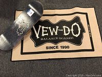 Photo showing Vew-do black balance board with skeleton figure logo and beige Vew-do branded mat with text.