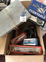 Box containing various vintage model train cars with Tyco branding and a gray box labeled 'Tracks' tied with string as well as a blue boxed turntable accessory.