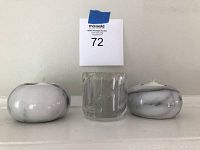 Three candles: two in round solid marble holders with gray/white marbling and one in clear glass holder with diagonal stripes.
