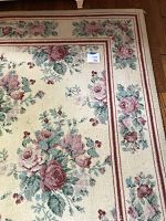 Close-up photo of a flowered area rug with pink and red roses and a bordered pattern in cream and rose colors.