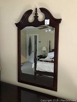 Front view of a large rectangular Thomasville mirror mounted on a wall. Shows ornate dark wood frame with carved top and central finial.