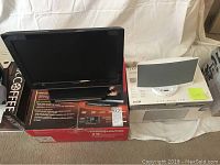 Magnavox 19-inch LCD TV sitting on its original box, next to a boxed Bose SoundDock speaker.