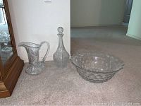 Three cut glass items displayed on carpet: bowl, pitcher, and decanter together