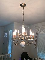 Ceramic hanging chandelier illuminated showing 10 flame-shaped candle lights and chain suspension from ceiling.