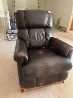 Full view of La-Z-Boy black leather lift chair showing the padded cushion and armrests, wood base, and wear on seating area.