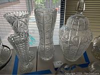 Three cut glass vases and one lidded jar arranged on a table showing different intricate cut glass patterns and shapes