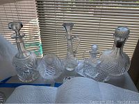 Full view of the six cut glass pieces including four decanters and two additional items showing various shapes and sizes on a tabletop.