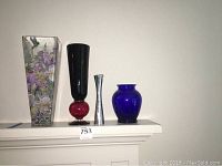 Wide shot showing all four glass vases on a mantle with a white wall background.