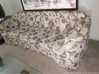 Side and front angled view of the vintage sofa showing curved armrest and floral upholstery pattern.