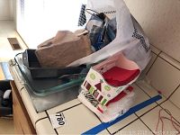Collection of kitchen items including pans, napkins, and lightbulbs stacked on white countertop.