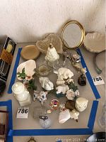 Collection of various home decor items including figurines, night lights, perfume bottles, condiment shakers, bowls, and a brass-framed mirror arranged on a table.