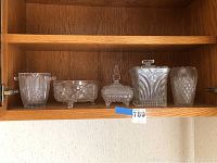Five glassware pieces displayed in wooden cabinet shelf including decanters, bowl, vase, and ice bucket.