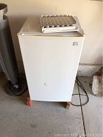 Front view of white Kenmore refrigerator with flat door, standing on wooden blocks in a garage.