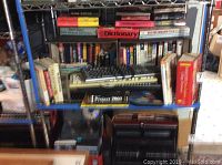 Shelf with multiple technical books and software, two keyboards tied with black cords in the center, and boxed software packages below keyboards.