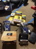 Photo showing three boxed Jabra EarWave Bluetooth headphones, two rapid chargers in packaging, Canon Coolpix camera box, battery charger, and two Canon Coolpix cameras with cases.