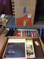 Wide shot of stacked boxes with automotive manual titles visible such as Chevrolet, Ford, and Jeep manuals, and showing overall quantity.