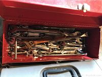 Red metal toolbox open displaying a variety of metal box end wrenches of different sizes neatly arranged inside.