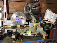 Full view of Porter Cable chop saw on workbench with extra 12 inch blade and some boxes around.