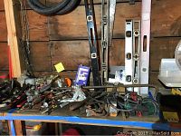 Table with various hand tools including levels, crowbars, and pliers spread out with some power tools visible.