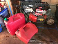 Mower and two gas cans with grass debris on tires and deck