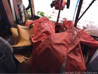 Photo showing multiple orange waterproof jackets and bib overalls along with three pairs of tall yellow rubber boots