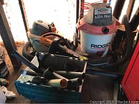 Photo showing Ridgid wet dry vac, Ridgid shop vac, Worx leaf blower and attachments in storage bin.