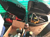 Two chainsaws in black hard cases with boxes and bottles of oil and other fluids around them.