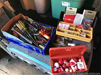 Photo showing three containers of fishing tackle and hand tools: red tackle box with fishing bobbers, yellow divided tackle box with fishing weights and hooks, blue crate with assorted screwdrivers, hammer, snips and safety glasses.