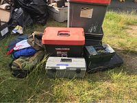 Photo shows six items including large gray bin with red lid, Task Force red and black tool box, green plastic box, small gray plastic box, large black bin, and some canvas bags on grass.