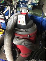 Full view of red commercial shop vacuum with attached hose in storage area.