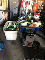 Wide shot of wheelbarrow and white bin holding various yard tools, small containers, and yard chemicals