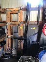 Wooden shelving frames stacked upright with metal folding stands and some other metal parts beside them, showing dismantled shelving components.