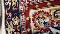 Close-up showing corner of a rug with red, cream, blue and gold ornate floral and geometric pattern.