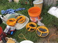 Image showing orange stacking tool bucket trays with screws and fittings placed on grass next to a large 5-gallon orange bucket.
