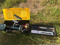 Open Stanley toolbox with yellow lid revealing carpet installation tools including knee kicker, blades, and pullers laid out.