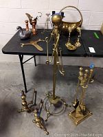 Brass towel stand, metal duck dish, copper pitcher, and other decorative accessories arranged on black table and beside it.
