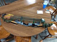 Full view of Bear AMO 44in compound bow laid on wooden table with 9 arrows placed on top.