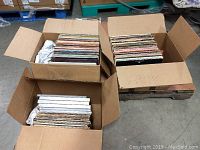 Three boxes filled with assorted vinyl LPs stacked upright in cardboard boxes on warehouse floor