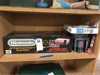 Shelf showing boxed Nintendo Entertainment System Action Set beside a stack of NES game cartridges and boxed SimCity game for Windows PC.