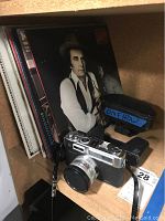 Yashica Electro 35 camera with lens cap and leather case sitting next to several vinyl LPs including one with a man's portrait wearing a white shirt and hat.