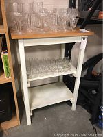 Wood kitchen island cabinet with cutting board top and various clear glassware on two shelves