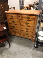 Front angle photo showing the entire light wood dresser with four drawers and brass handles, visible scratches on top.