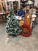 Full view of the 4-foot faux Christmas tree with white-tipped branches, wooden sled, and red berry wreath in a sale setting.