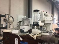 Overview photo showing several appliances on wooden chest including mixers, blender, food processor and coffee machine.