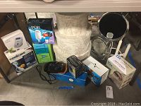 Overall lot view showing multiple boxed items, various cameras, hat boxes, mirrors, and other health and personal care products under the table.