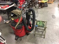 Photo of the red Craftsman wet dry vacuum with flexible black hose and attached gas mask. Next to it is a small folding stool with camouflage fabric seat and wooden olive green frame.