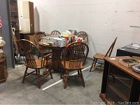 Full view of entire oak dining set including six chairs surrounding the round table in warehouse setting.