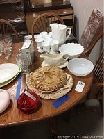 Wide view of assortment on wooden table showing milk glass pitcher, eight goblets, bowls, glass candy dish, pie keeper, gravy boat, and glass dish.