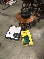 Photo of all items in the lot: wood side table, cast iron moose on top, Glacier Bay toilet seat box, and hanging file folders box on the floor.