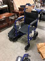 Side and angled view of blue Excel aluminum wheelchair showing black fabric seat and travel bag on floor